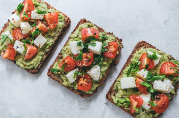 Bruschetta toast with guacamole and tomatoes, sea salt and herbs on dark bread, healthy nutrition. Close up