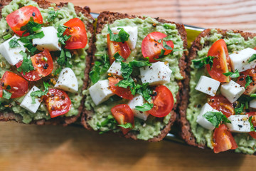 Bruschetta toast with guacamole and tomatoes, sea salt and herbs on dark bread, healthy nutrition. Close up