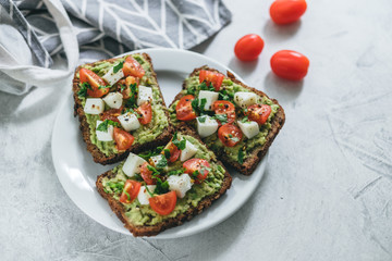 Bruschetta toast with guacamole and tomatoes, sea salt and herbs on dark bread and a white plate, healthy nutrition.