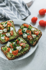 Bruschetta toast with guacamole and tomatoes, sea salt and herbs on dark bread and a white plate, healthy nutrition.