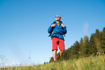Fototapeta premium Middle-aged Backpacker traveler looking at sunset and preparing for trekking at summertime sunny day. Active people concept image.