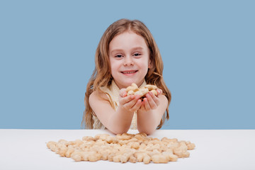 portret of little girl with Peanut in hand isolated on blue background, sitting at a table