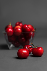 Selective focus, photograph of a glass container full of cherries, on a dark grey background.