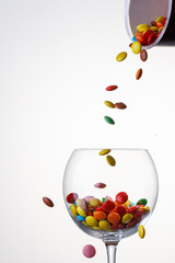 sweet colorful Candy coated chocolate falling in to a glass on white background.