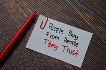 People Buy From People They Trust write on sticky note isolated on wooden table.