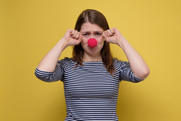 Unhappy young woman pointing with red clown nose crying, looking sad