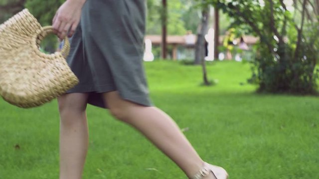 Side view of Young woman with handmade stylish straw handbag walks in the summer park. Eco bag.