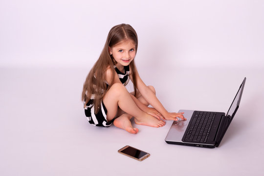 Emotional portrait of an enthusiastic and quick-witted beautiful little girl, with interest clicking on a laptop keyboard while playing isolated on white background
