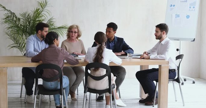 Full length skilled middle aged beautiful female manager sharing project ideas, discussing working issues with motivated young mixed race diverse colleagues at brainstorming meeting in boardroom.