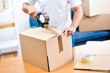 Worker hands holding packing machine and sealing cardboard or paper boxes
