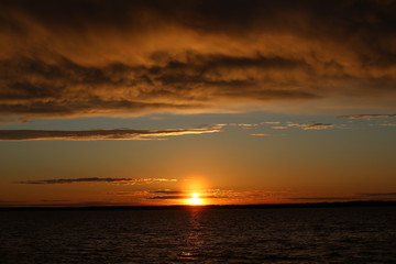 A fire is burning in the sky at sunset with lush illuminated orange clouds covering half of the clear horizon.The last glimmer near the lake.A striking contrast picture at the end of the day.Russia