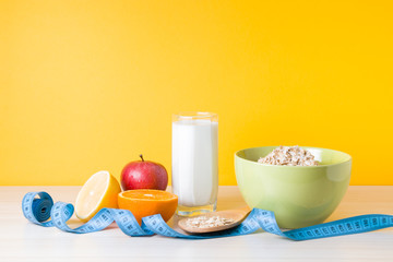 glass of milk, fruits, a bowl of oatmeal and a blue measuring tape on the table, yellow background, healthy lifestyle concept, proper nutrition and weight loss