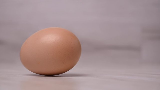 Close-up of a female cook laying a chicken egg on the kitchen table. 4K