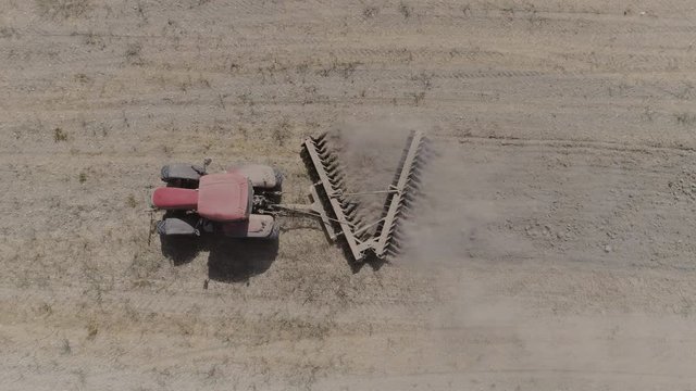 AERIAL DRONE TOP DOWN ZENITHAL SHOT OF VINTAGE TRACTOR PLOWING IN ARID AGRICULTURE FIELD WITH DUST 