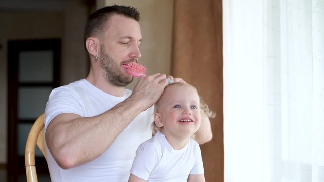 Father and little daughter have fun together. Dad does a hairstyle to his daughter. Combing hair. close up