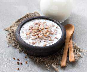 Milk buckwheat soup in a wooden bowl in rustic style on a light gray background