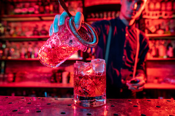 Close up of professional barman finishes preparation of alcoholic cocktail in multicolored neon...