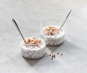 Breakfast buckwheat boiled with milk in a glass Cup on a light gray background