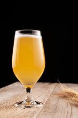 Glass of homemade craft beer on a wooden table. Nearby are barley spikelets. Close-up, copy space. Dark background. Vertical orientation
