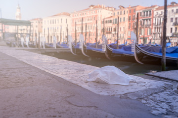 surgical mask on the ground near to some docked gondolas on grand canal in venice
