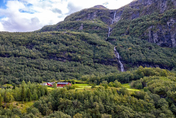 Obraz na płótnie Canvas Norwegian farm at the foot of the mountain against the waterfall