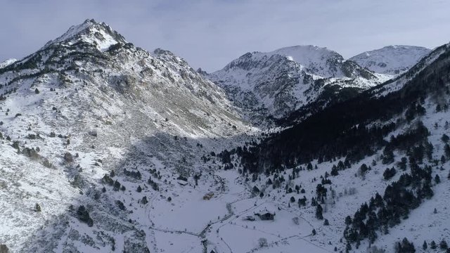 AERIAL DRONE BACKWARD SHOT THROUGH SNOWED VALLEY IN ANDORRA, ROCKY MOUNTAIN AND WOODS IN THE PYRENEES