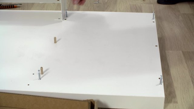 Close up view of handyman attaching wooden pegs in particle board. Cropped view of man assembling furniture at home. Home improvement concept