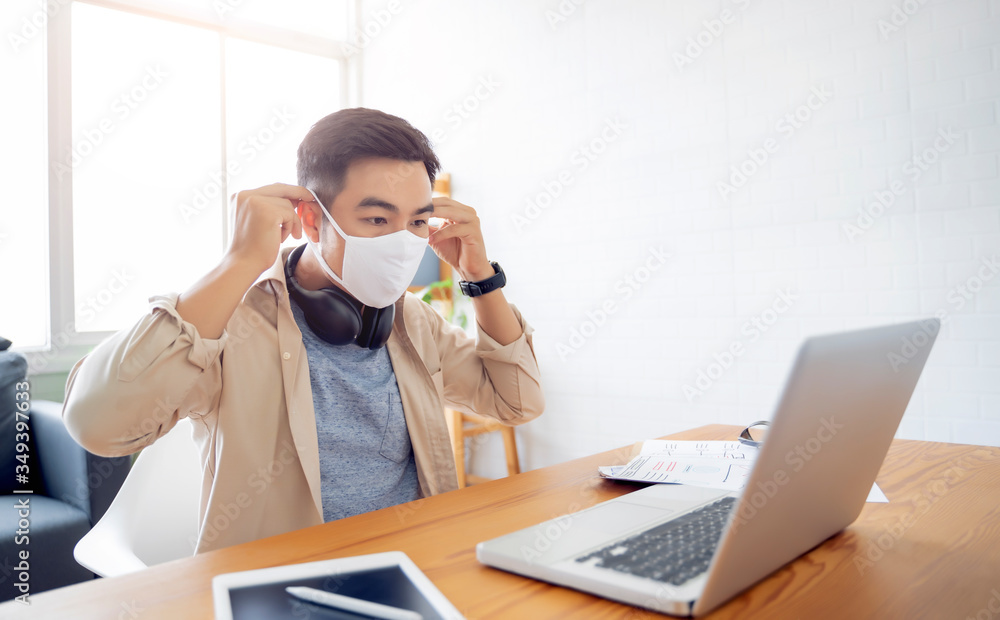 Fototapete Asian man putting on protective mask Working from home web designing graphical user interface UX UI, in home office using computer laptop designing creative planning innovative idea, in quarantine
