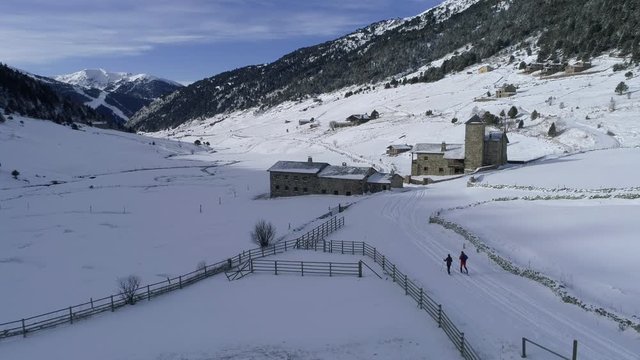 AERIAL DRONE ORBIT SHOT OF COUPLE PRACTICING CROSS COUNTRY SKYI IN BEAUTIFUL SNOWED VALLEY IN ANDORRA, THE PYRENEES. 