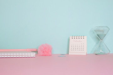 Side view on a still life. Pink fluffy pen, notepad and calendar on a pink table. Turquoise wall on the back