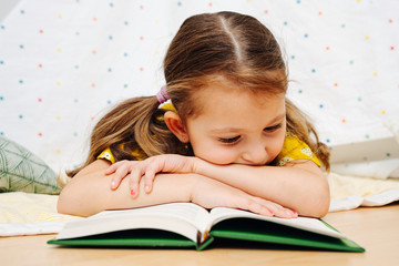 Entertained little girl keen on reading book while lying on the floor.