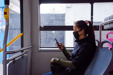 A young woman wearing a mask and uses her smartphone on public transport