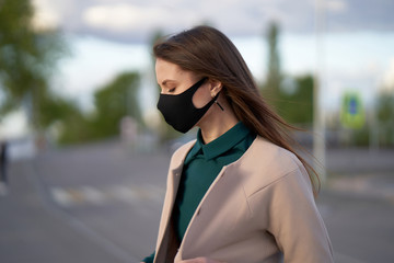 Beautiful girl in a black medical mask with closed eyes on the street during a coronavirus epidemic.      