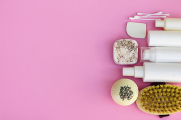 White cosmetic bottles, bath bomb, handmade soap, bath salt, massage brush, sponge, cotton buds with cherry flowers on a pink background. Natural organic cosmetics concept.