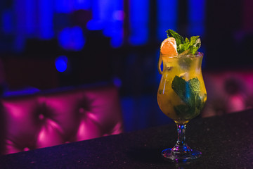 Copa coctel naranja yerbabuena sobre barra de bar fondo azul.