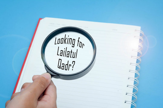 Finding Lailatul Qadr concept. "Looking For Lailatul Qadr" A through magnifying glass and a book over turquoise background. Lailatul Qadr the special night of the last ten days of Ramadan. 