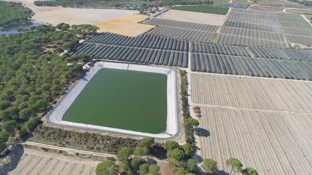 AERIAL DRONE ORBIT OF INDUSTRIAL AGRICULTURE WATER TANK FOR IRRIGATION IN GREEN FIELDS. FINAL TILT-UP AND HORIZON

