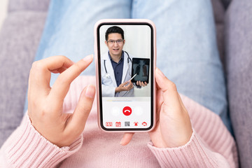 Asian chinese doctor video conference call online live talk follow up remotely in medical coronavirus result with woman sit on sofa couch at home using online doctor consult service on smartphone.