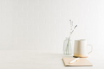 Straight on view of clean, minimal desk with coffee mug, notebook and glass vase
