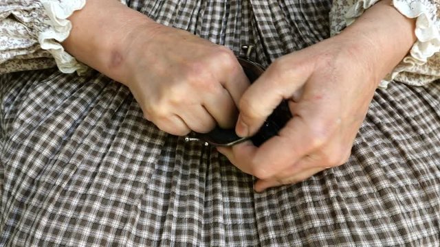 Wrinkly hands of mature adult woman in rustic dress takes of black leather wallet and count some different small coins in palm of her hand. Concept of poverty and financial crisis. Close up.