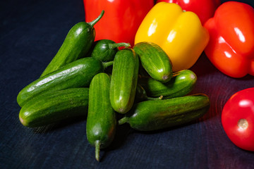 Cucumbers, tomatoes and peppers on a dark table. Bright vegetables on dark background. Fresh vegetables. Vitamin salad. Vegetarianism. Vegans. A raw food diet. Vegetable shop.