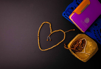 Isolated Muslim prayer beads. Wicker basket and quran fordable book rest. Low key and focus on beads on table. Arabic calligraphy and non-English means the quran and its translations.