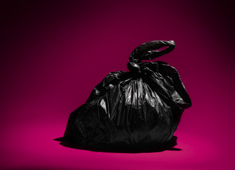 Black rubbish bin trash bag on a vibrant purple /pink background. Half full of waste,  plastic...