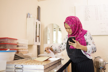 woman in her workshop baking some cake and checking her product using mobile phone