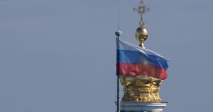 The Russian flag sways in the wind against the background of the Golden Dome of the Hermitage. The Winter Palace and the Russian flag in Saint-Petersburg against the sky.