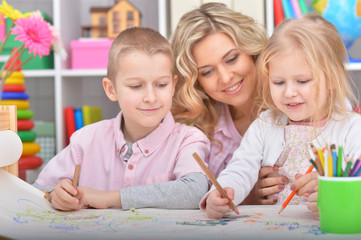 Fototapeta premium Portrait of mother with cute children drawing with pencils at home