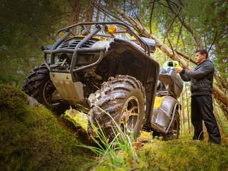 ATV. A man puts on a helmet against the background of a Quad bike. A man is going to ride an ATV on a forest road. Transport for hard-to-reach places. Extreme travel.