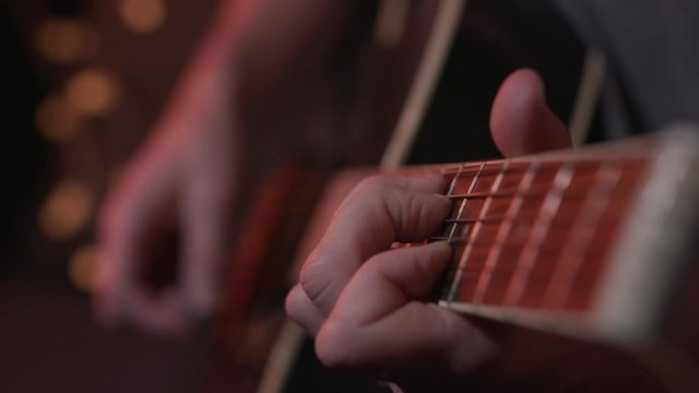 Man plays chords on an acoustic guitar in a studio, cinematic lighting