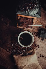 coffee mug surrounded by a filled vintage coffee grinder, spilt burlap sack of coffee beans and...
