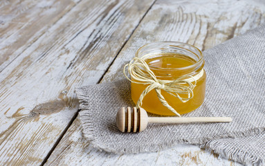 small glass jar of honey with a wooden spoon close-up on a wooden background in a rustic style.